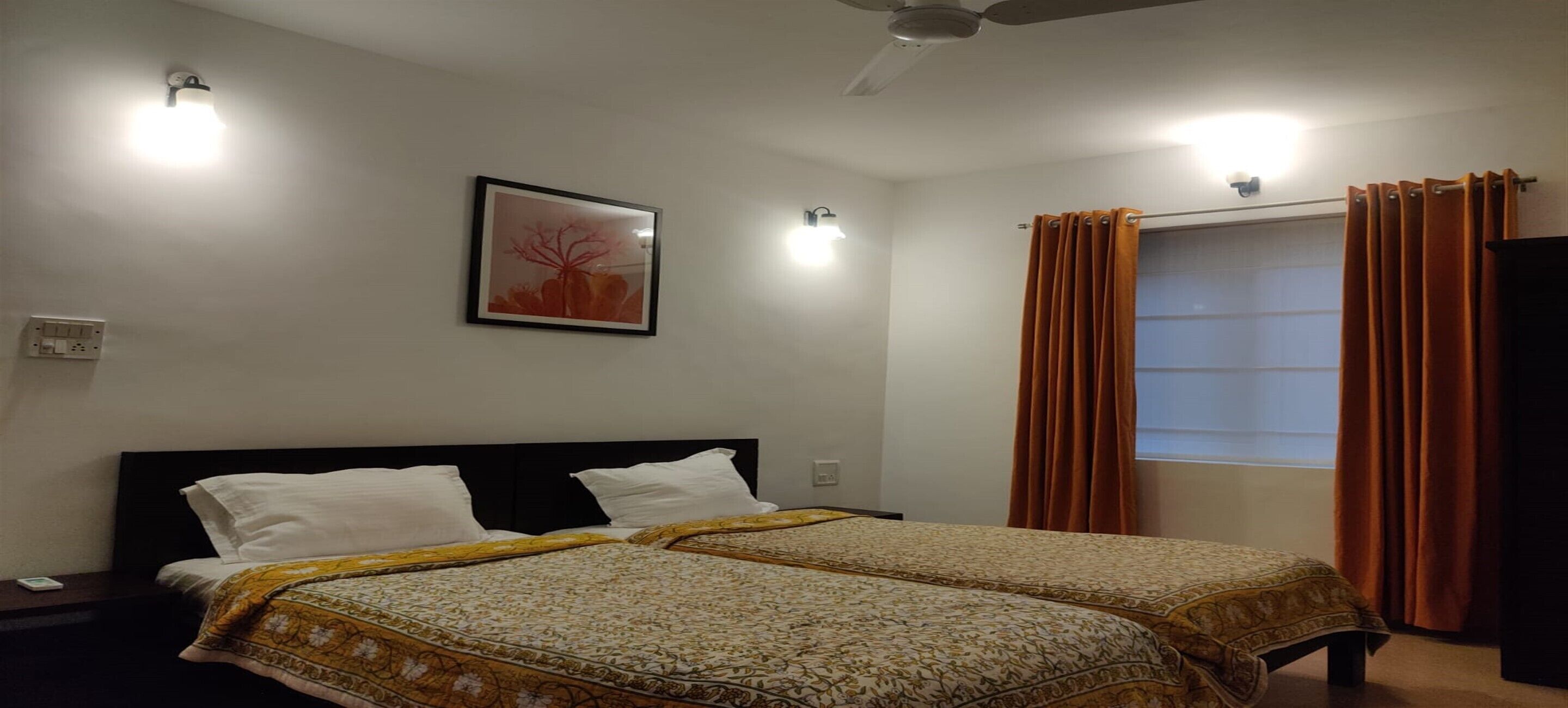Habitación de hotel con dos camas, ventilador de techo, un cuadro enmarcado en la pared y una ventana con cortinas.