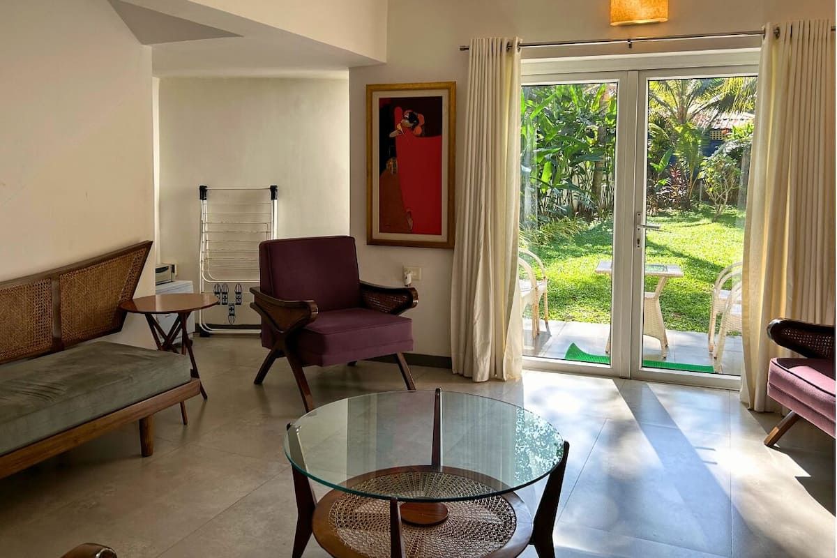 A living room with a glass table, a sofa, a chair, and a view of a garden through a sliding door.