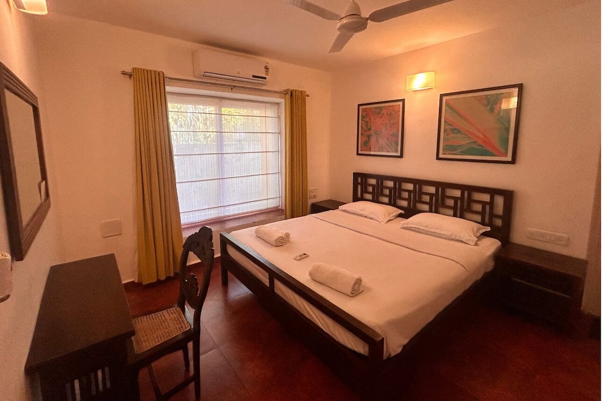 A hotel room with a bed, a desk, a chair, a ceiling fan, and artwork on the walls.