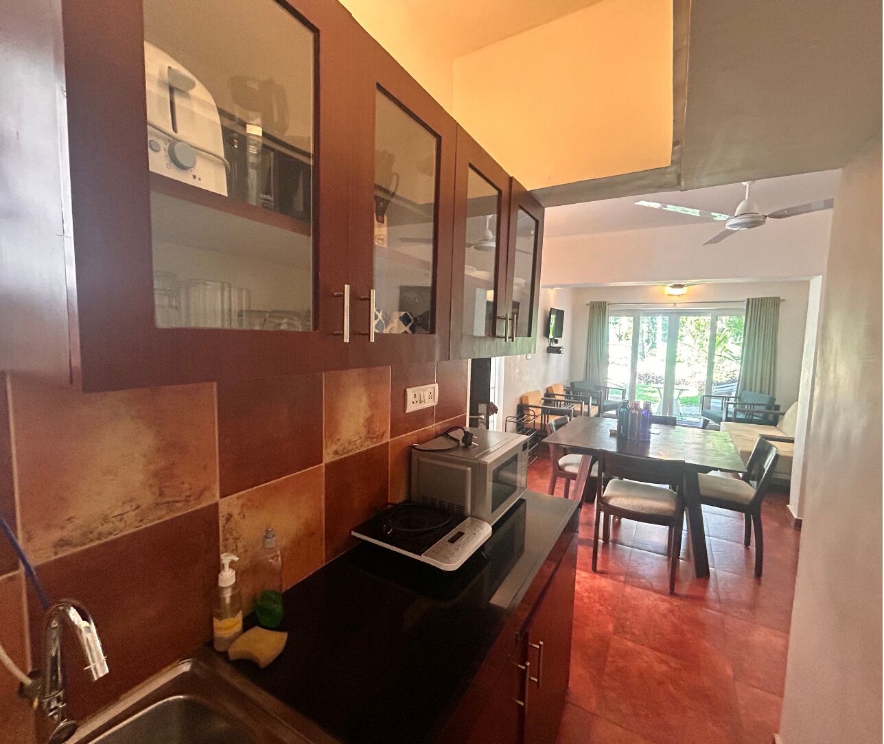 Cocina compacta con microondas, lavabo y armarios. Zona de comedor con mesa y sillas.