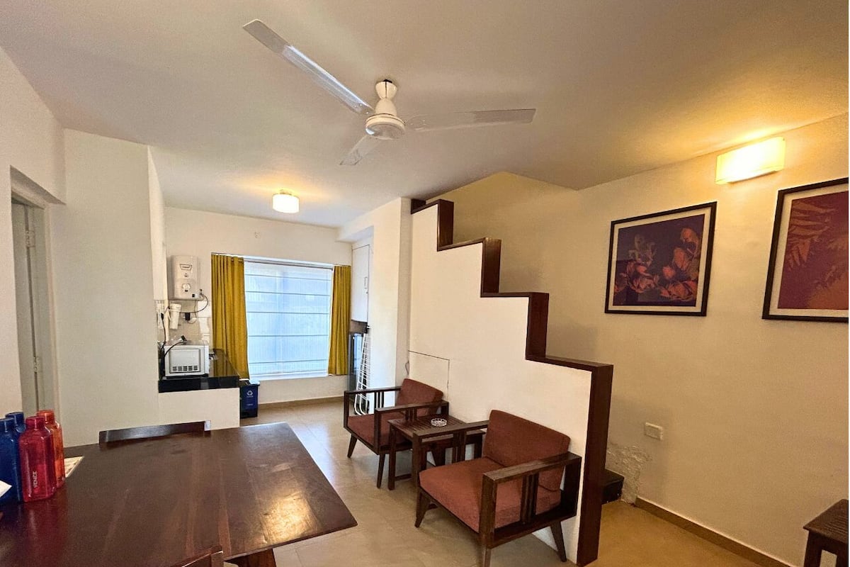 A dining area with a wooden table and chairs, a staircase, and a kitchen in the background.