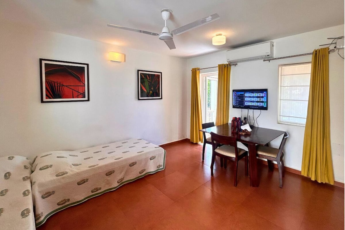 A room with a bed, a dining table with chairs, a ceiling fan, and a flat-screen TV.