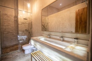 Une salle de bain moderne avec une douche à l’italienne en verre, un meuble-lavabo en marbre et un grand miroir.