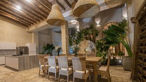 Una cocina amplia con electrodomésticos modernos, un comedor con sillas de mimbre y una mesa de madera, y una planta grande en maceta al fondo.