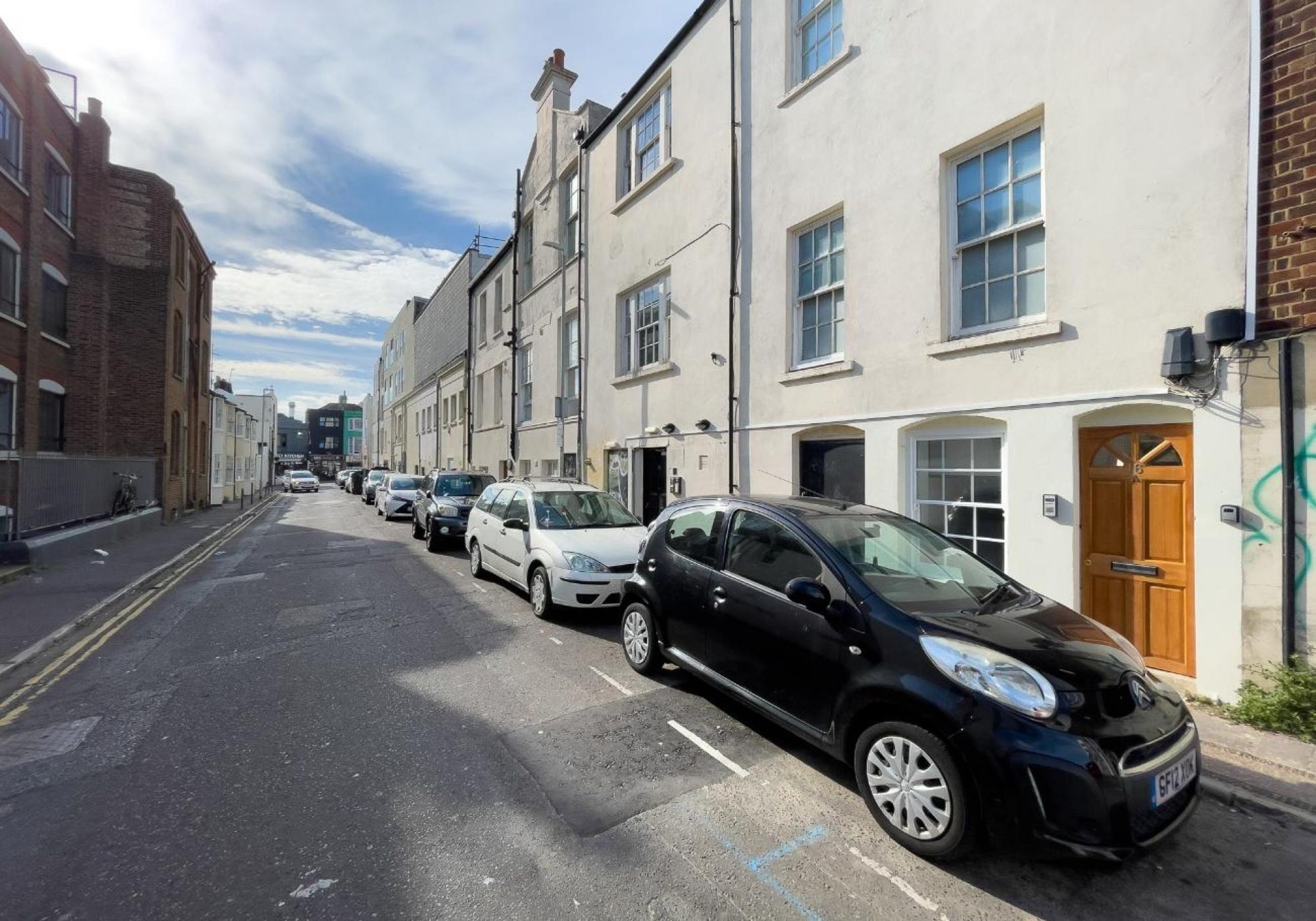 Une rue bordée de voitures garées et d’immeubles.