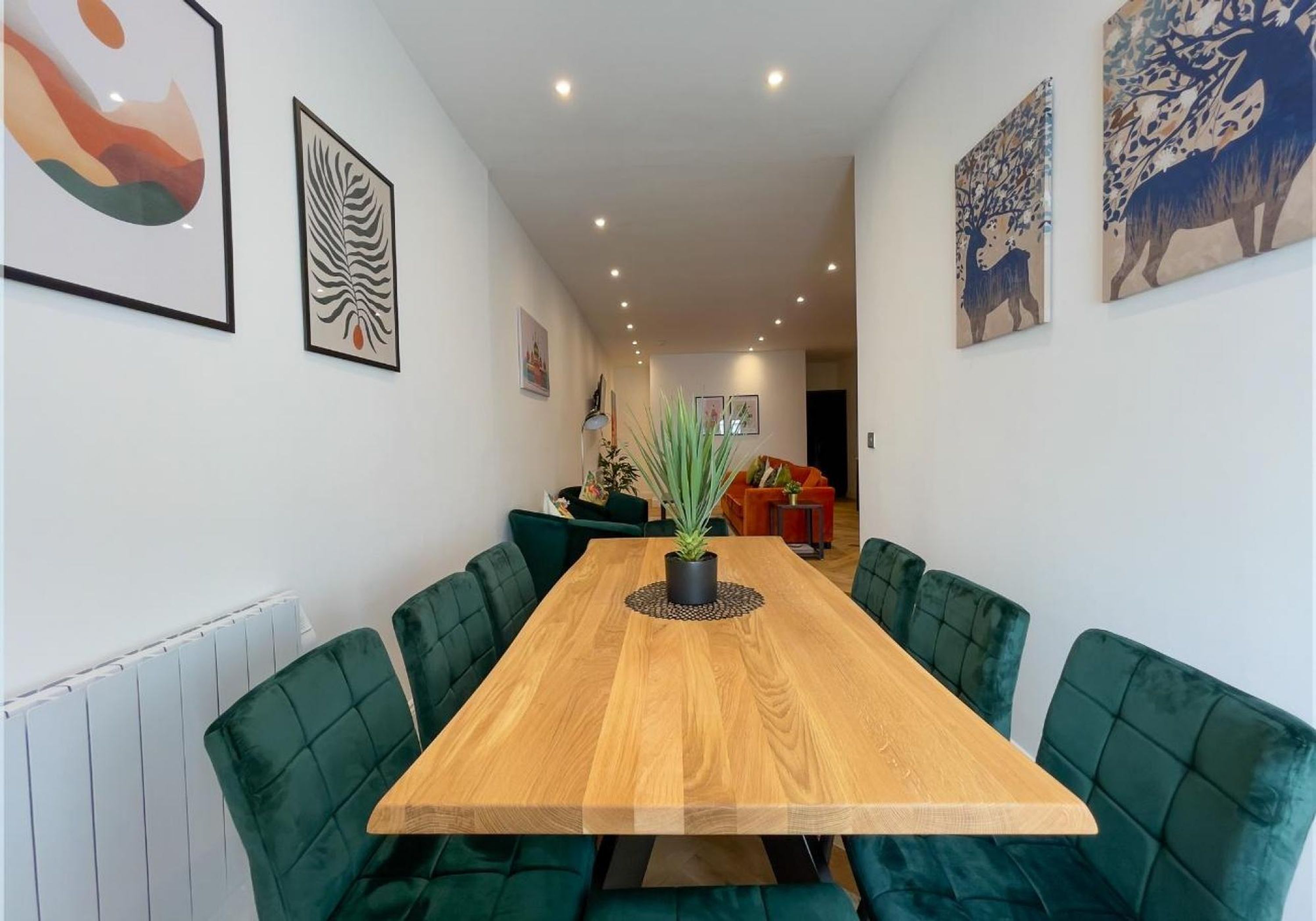 A dining area with a wooden table and green upholstered chairs, surrounded by walls with framed artwork.
