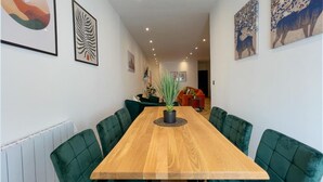 Ein Essbereich mit einem Holztisch und grünen, gepolsterten Stühlen, umgeben von Wänden mit gerahmten Kunstwerken.