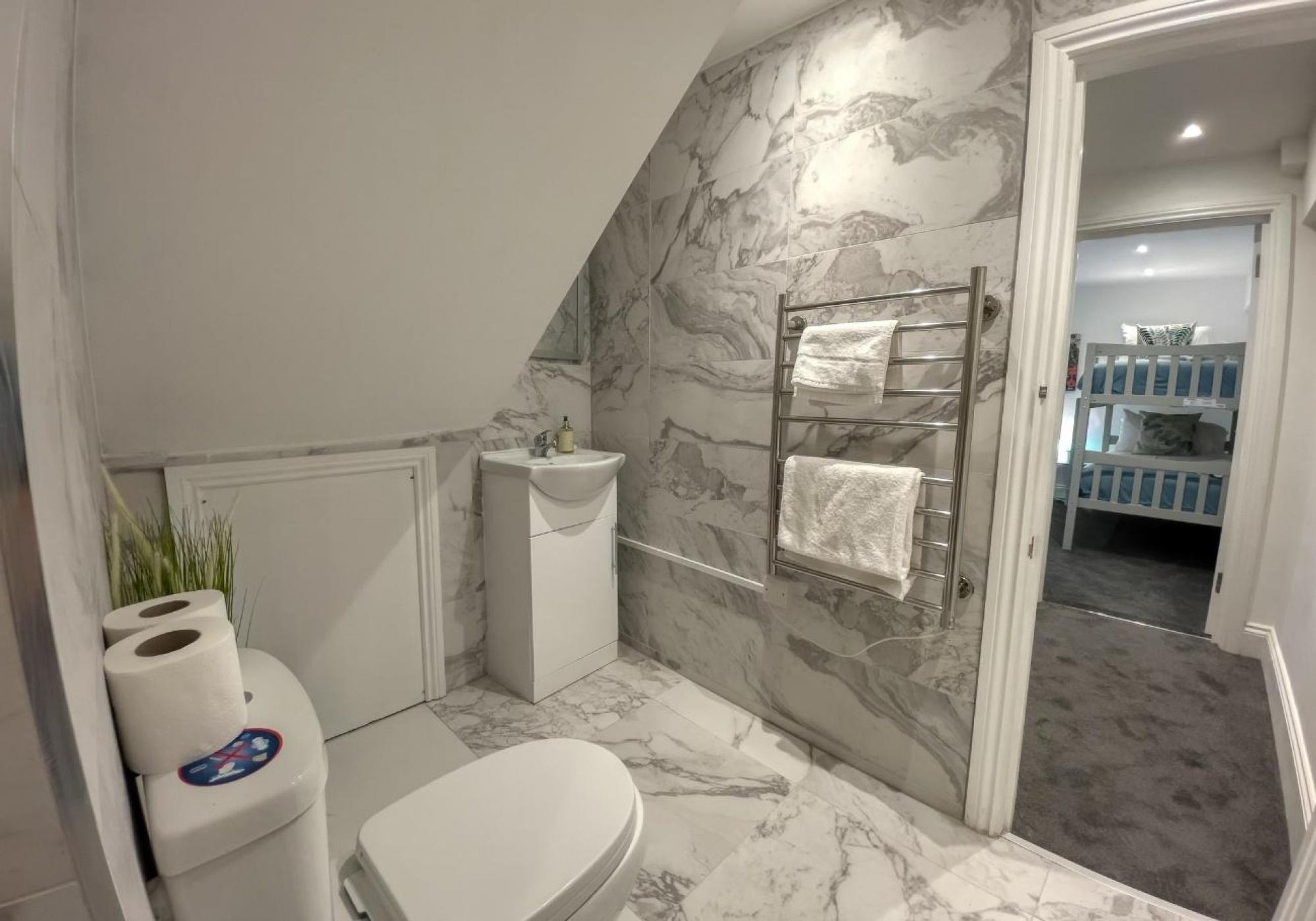 A bathroom with a toilet, sink, and towel rack against marble walls.