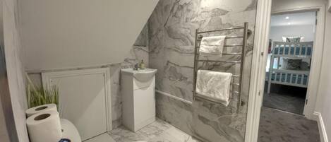 A bathroom with a toilet, sink, and towel rack against marble walls.