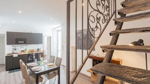 A modern kitchen with dark cabinets, a dining area with a wooden table and chairs, and a staircase with a decorative metal railing. - Via Muralto 13 in Como (Como)