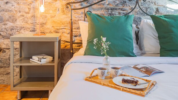 A neatly made bed with green and white pillows, a bedside table with a lamp, a tray with a cake slice, and a book. - Via Muralto 13 in Como (Como)