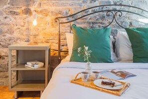 Un lit bien fait, avec des oreillers verts et blancs, une table de chevet avec une lampe, un plateau avec une part de gâteau et un livre.