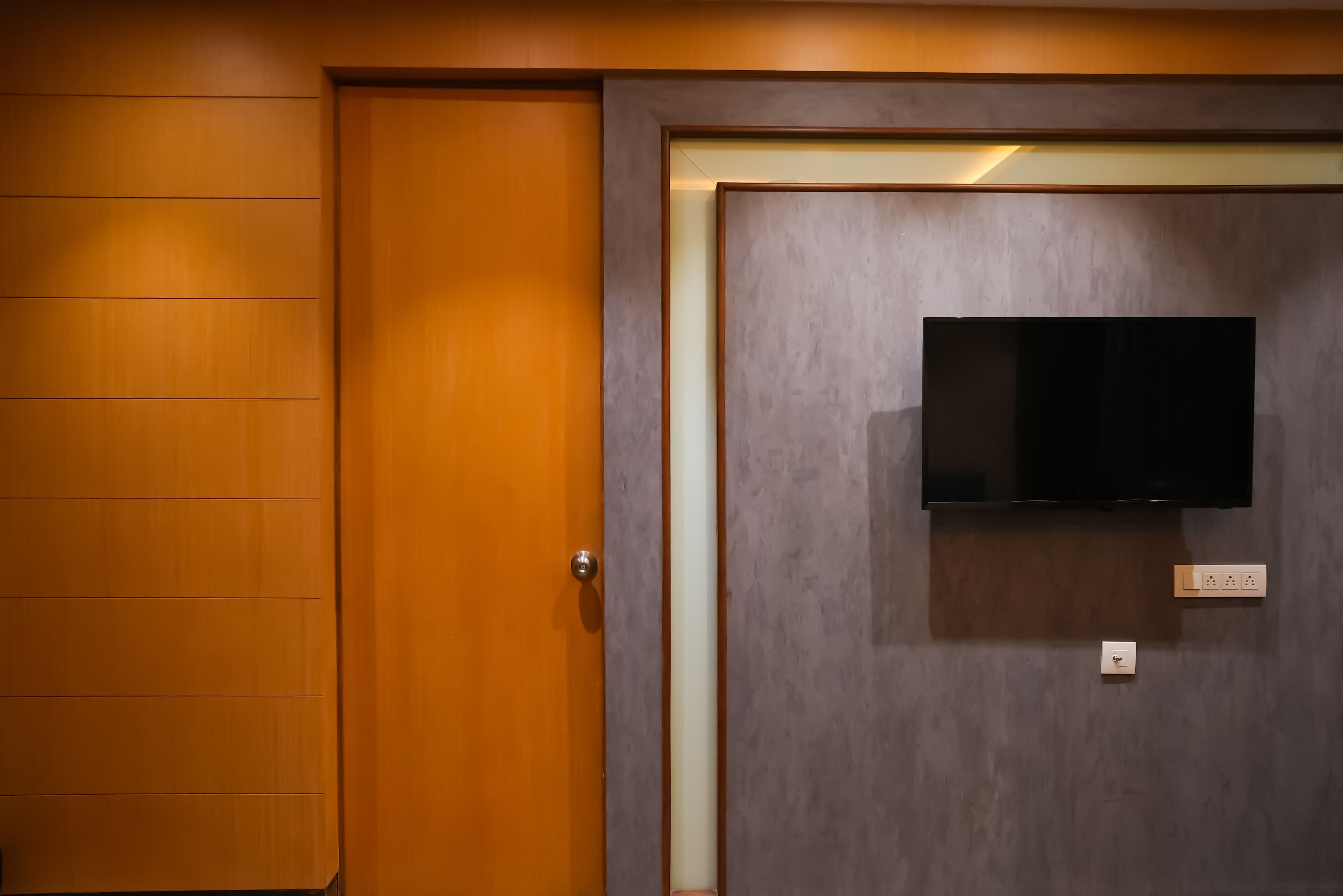 A room with a wooden door and a wall-mounted television.