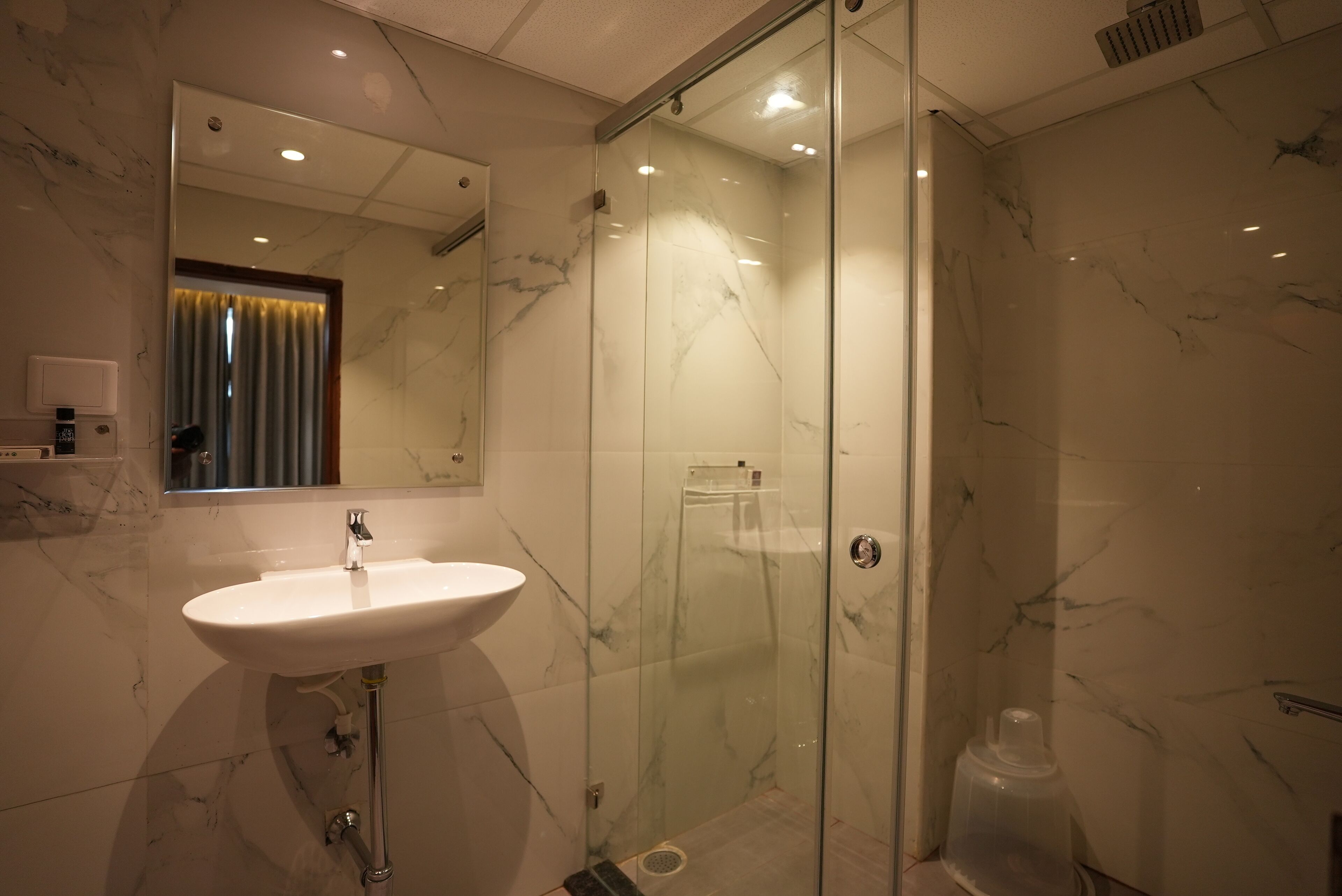 Un baño moderno con ducha de vidrio, pared de azulejos de mármol y lavamanos blanco.
