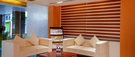 A reception area with two white sofas, a wooden coffee table, and a reception desk with a menu board.