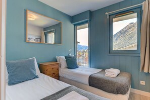 Una camera da letto con due letti, una cassettiera in legno, uno specchio e una finestra con vista sulle montagne.