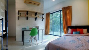 A bedroom with a bed, a desk with a chair, a window with curtains, and a brick wall with shelves. - Industrial Suites at Bandar Sunway (Petaling Jaya)