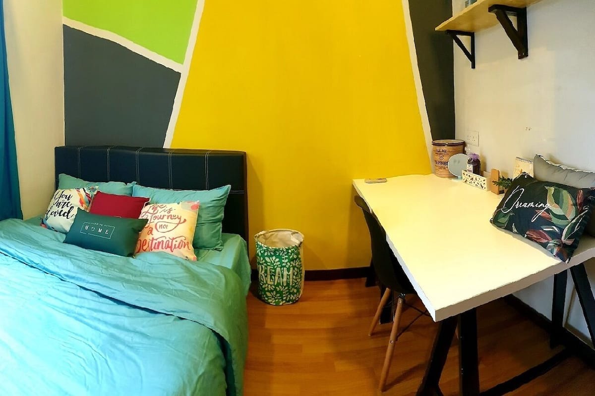 A small, brightly colored room with a bed, a desk, and a window.