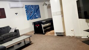 A living room with a black sofa, a glass coffee table, a treadmill, a TV, and a wall-mounted air conditioner. - Port of Sale, town centre 5KM drive (Wurruk)
