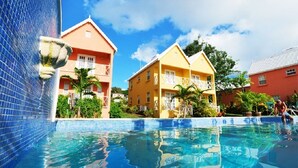 A swimming pool with a tiled edge, surrounded by buildings with balconies and a clear blue sky. - Villa located in St James on the west cost of Barbados with sea view and pool. (Fitts Village)