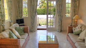 A living room with two wicker sofas, a glass coffee table, a television, and a lamp. - Villa located in St James on the west cost of Barbados with sea view and pool. (Fitts Village)