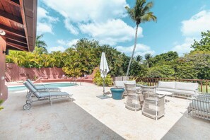 A poolside area with lounge chairs, a table, and a sofa.