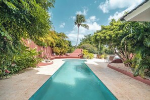 Une piscine à bord incurvé, entourée d’une végétation luxuriante et baignée par un ciel dégagé.
