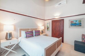 A bedroom with a bed, bedside lamps, a wooden door, and a painting on the wall.