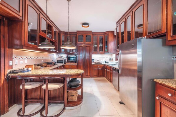 A kitchen with wooden cabinets, a stainless steel refrigerator, and a bar area with stools.