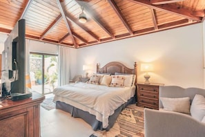 Un dormitorio con techo de madera, una cama grande, lámparas de noche, televisor y vistas al exterior.