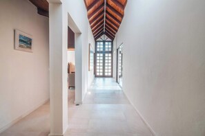 Un couloir avec un plafond haut, des murs blancs et un escalier en bois.