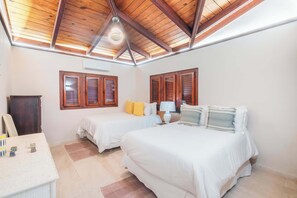 Une chambre avec deux lits, des poutres apparentes en bois au plafond, un ventilateur de plafond et une fenêtre avec des volets.