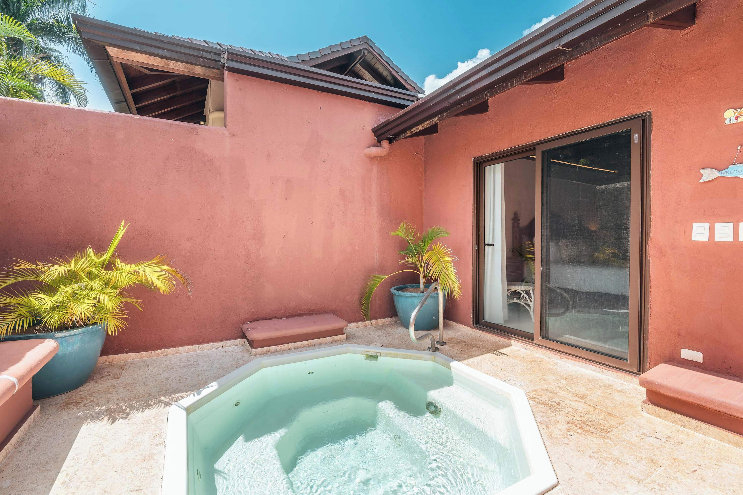 Una piscina con un jacuzzi, rodeada por un edificio rojo con puerta de vidrio corredera.