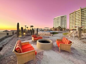 Un resort con mesas al aire libre, piscina y un edificio grande al fondo.