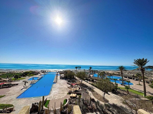 Un resort con varias piscinas, palmeras y vista al océano.