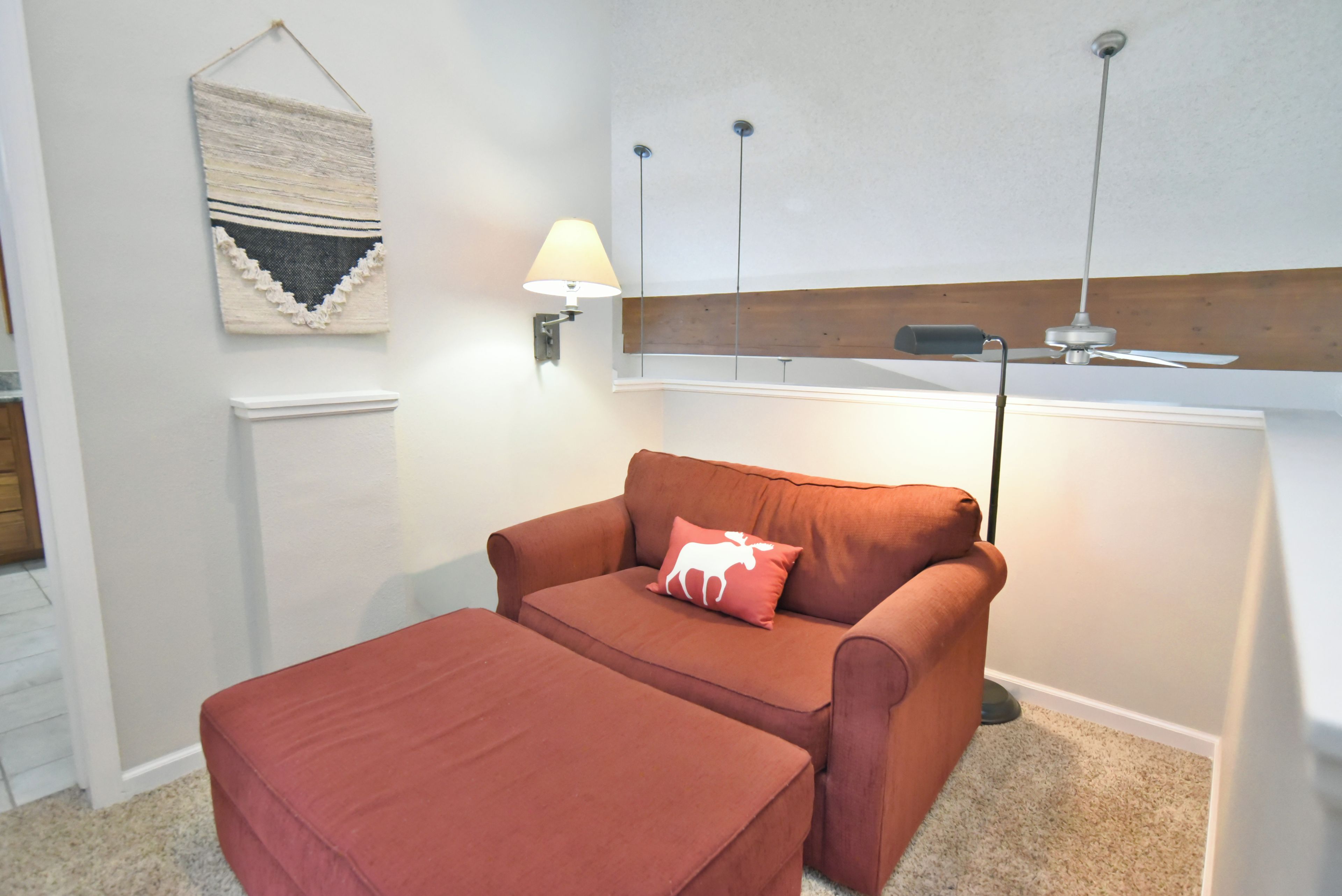 Una habitación con un sofá marrón, un reposapiés a juego, una lámpara de pared y un ventilador de techo.
