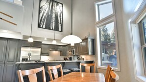 Una cocina moderna con armarios oscuros, una mesa de comedor de madera e iluminación colgante.