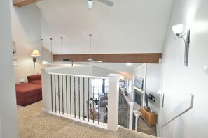 Un vaste espace de vie doté d’un haut plafond, d’un ventilateur de plafond et d’un escalier menant à un niveau supérieur.