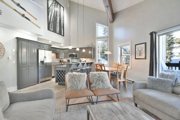 A modern kitchen with stainless steel appliances, a dining area with wooden chairs, and a cozy seating area with plush cushions.