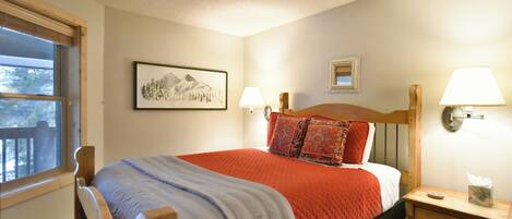 A bedroom with a bed, bedside lamps, a nightstand, a window, and a framed picture on the wall.