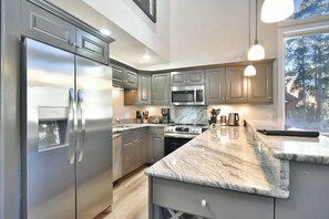 A modern kitchen with stainless steel appliances, granite countertops, and a large window offering a view of trees.