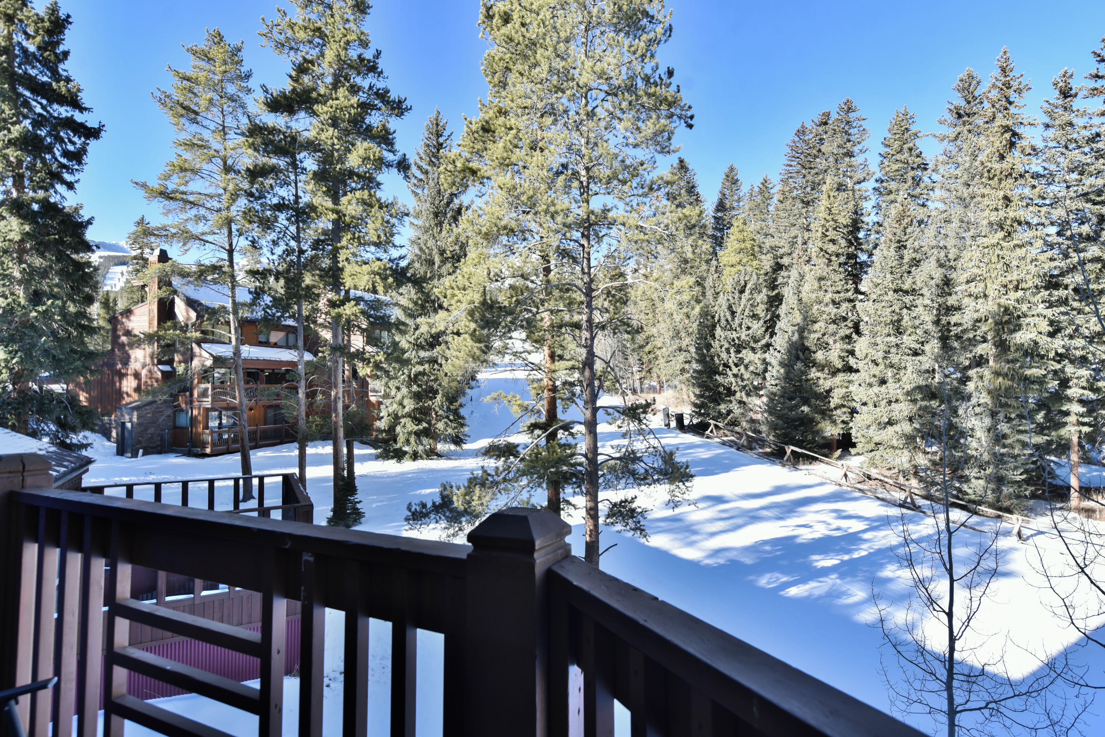 A snow-covered landscape with a wooden deck and a view of a lodge in the background.