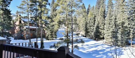 A snow-covered landscape with a wooden deck and a view of a lodge in the background.
