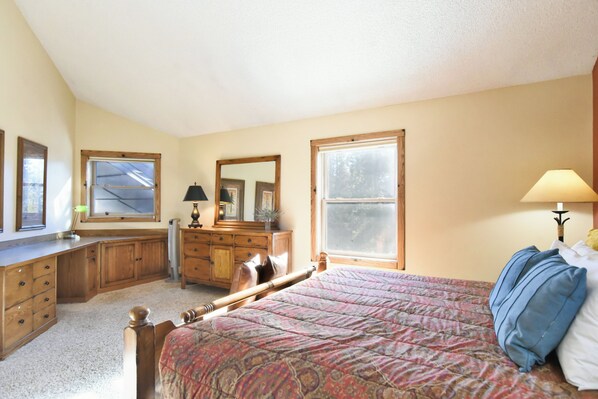 A bedroom with a bed, dresser, mirror, and two windows.