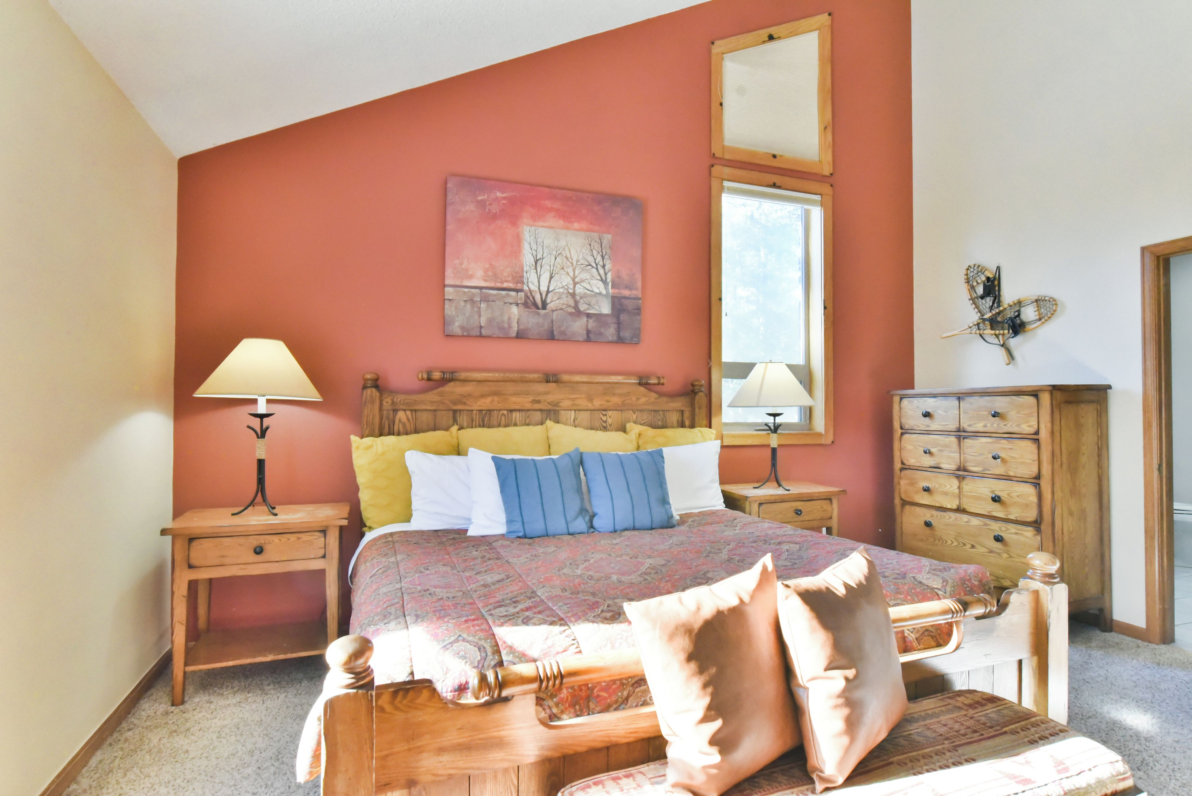 A bedroom with a bed, two bedside tables, a dresser, a painting on the wall, and a window.