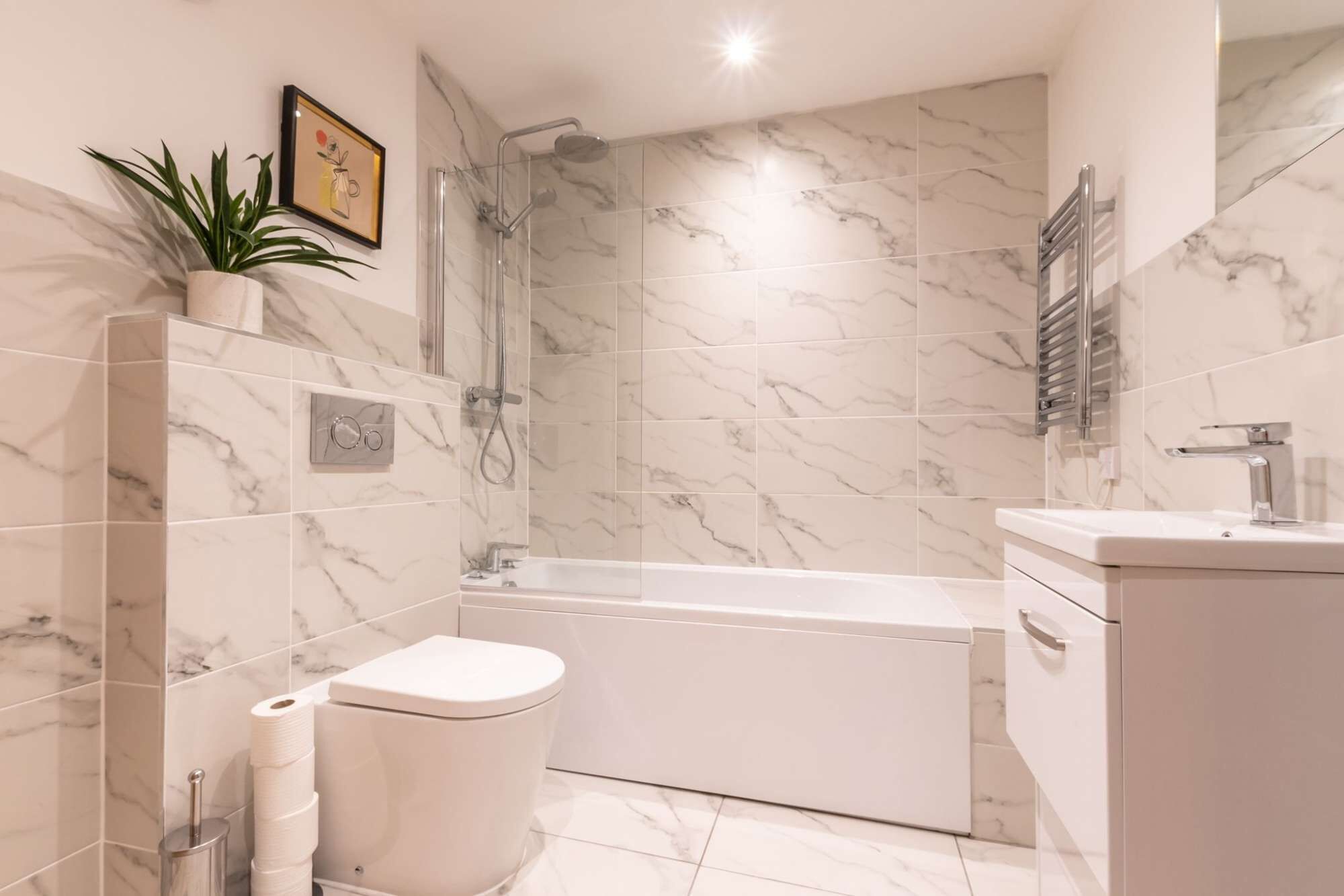 A modern bathroom with a toilet, bidet, shower, and bathtub, all with marble tiles.