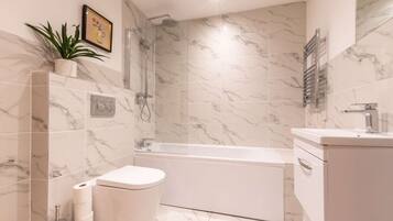 A modern bathroom with a toilet, bidet, shower, and bathtub, all with marble tiles.