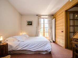 Ein Schlafzimmer mit einem Bett, einem Nachttisch, einem Fenster mit Vorhängen und einer Holzwand.