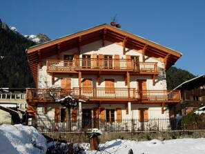 Ein mehrstöckiges Gebäude mit Balkonen, einer Steinaußenwand und einer Bergkulisse.