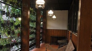 A wooden bench in a room with a tiled floor, a wooden wall, and a hanging light fixture. - Bamboe Inn 2 Homestay (Bandar Lampung)